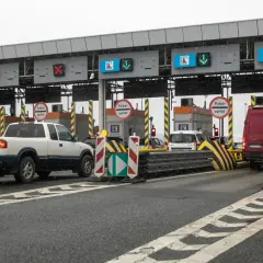 Autostrada z bramkami, znaki "Pobór opłat", czerwone krzyżyki i zielone strzałki nad pasami ruchu.
