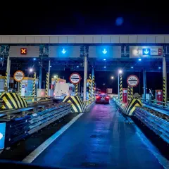 Nocny widok na bramki poboru opłat na autostradzie z niebieskimi światłami i znakami.