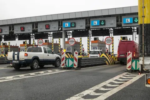 Autostrada z bramkami, znaki "Pobór opłat", czerwone krzyżyki i zielone strzałki nad pasami ruchu.