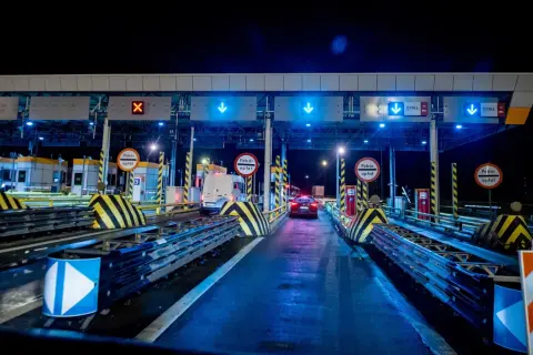 Nocny widok na bramki poboru opłat na autostradzie z niebieskimi światłami i znakami.