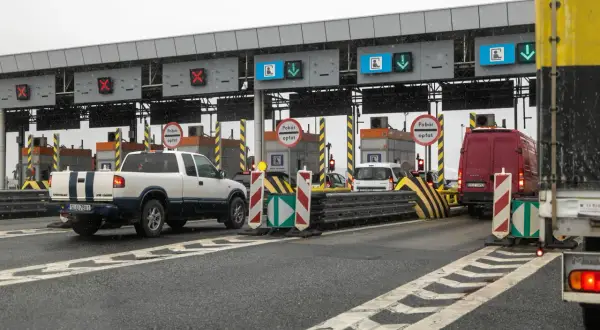 Autostrada z bramkami, znaki "Pobór opłat", czerwone krzyżyki i zielone strzałki nad pasami ruchu.