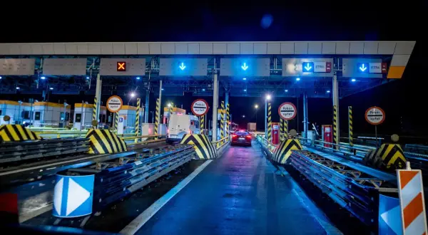 Nocny widok na bramki poboru opłat na autostradzie z niebieskimi światłami i znakami.