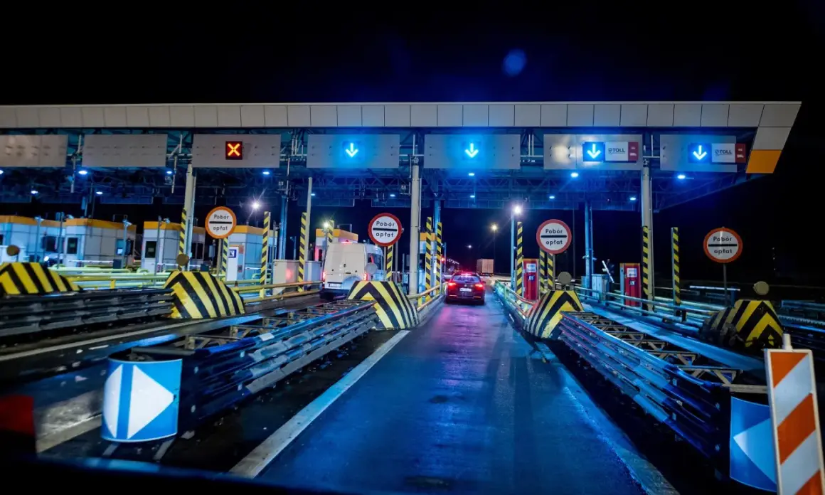 Nocny widok na bramki poboru opłat na autostradzie z niebieskimi światłami i znakami.
